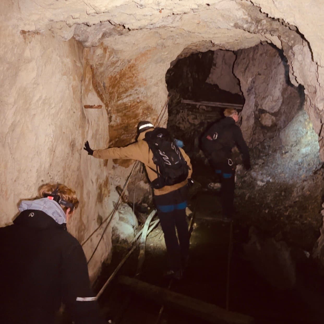 Tre personer med hodelykter utforsker en grotte