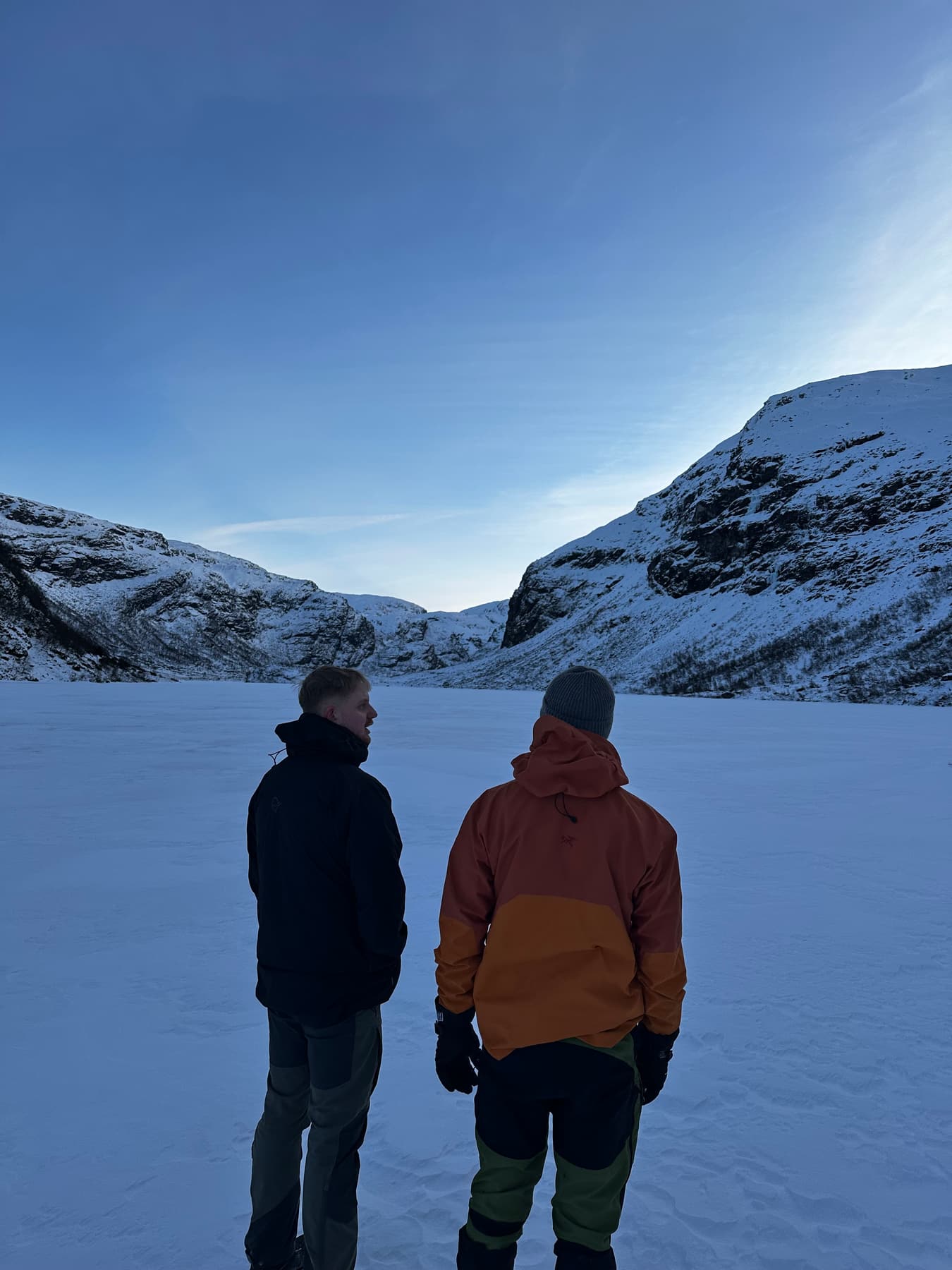 To personer på et islagt fjellvann med snødekte fjell
